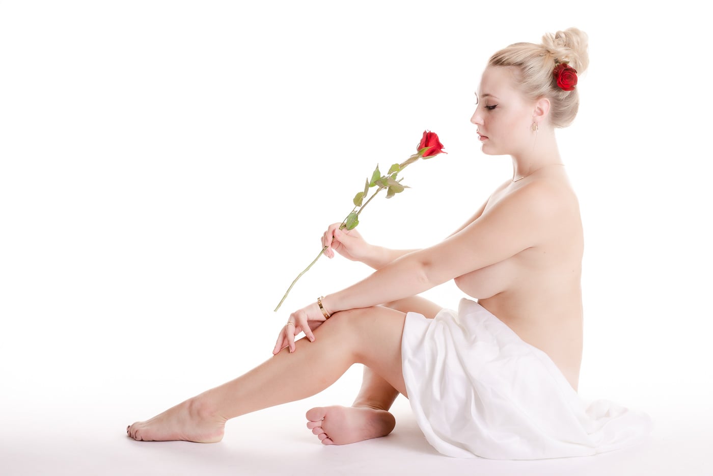 Ung nøgen kvinde siddende på gulvet, som dufter til en rød rose